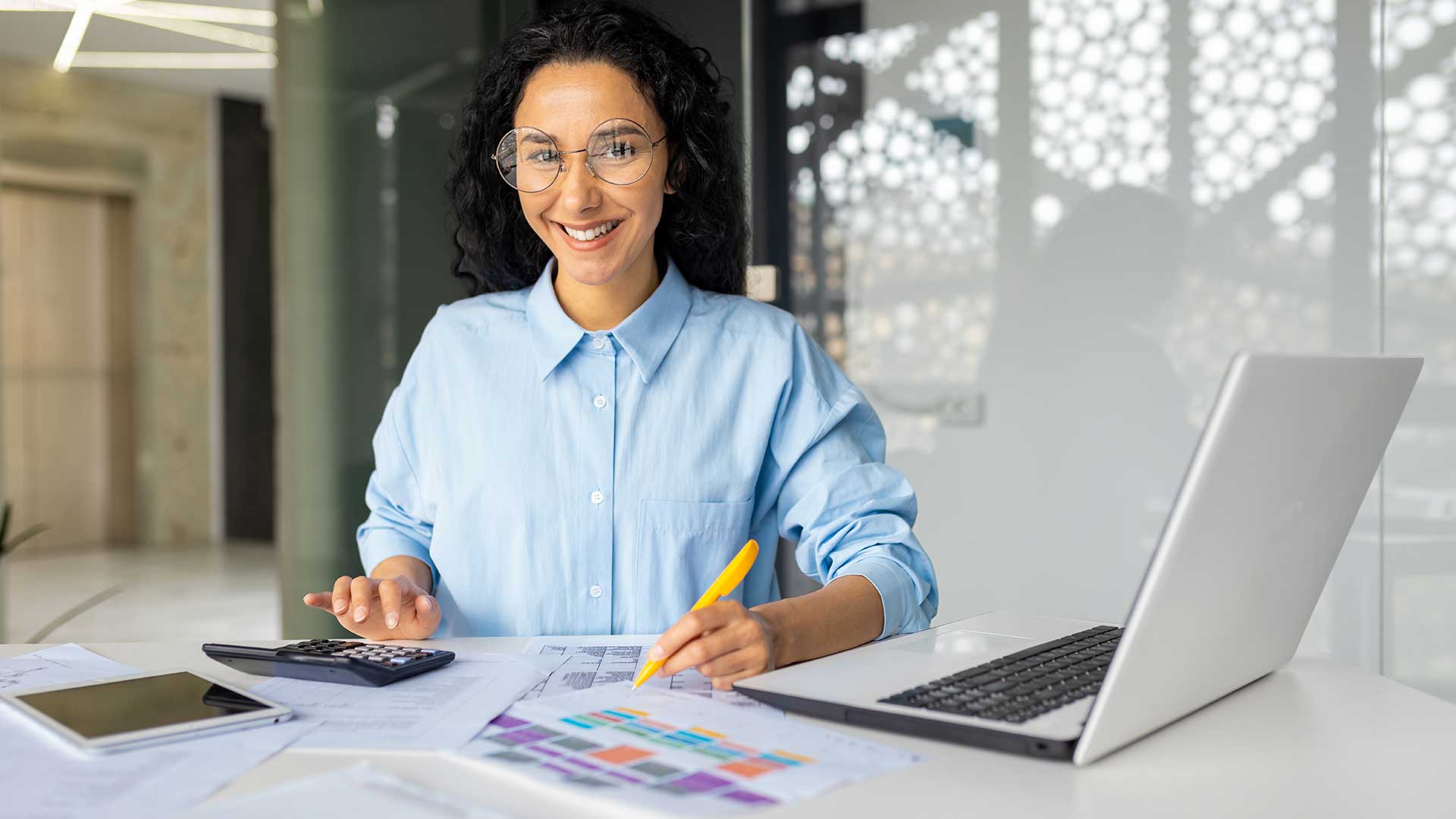 a woman in accounting department smiling at a desk with a calculator and pen